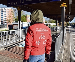 Am Elmshorner Bahnhof steht ein Reisendenhelfer auf dem Bahnsteig zwischen den Gleisen 2 und 3. Er bietet Fahrgästen mit schweren Koffern, Kinderwagen und E-Bikes seine Hilfe an. Im Hintergrund sind die Bretterwände zu sehen, mit denen der Fahrstuhlschacht abgesperrt ist – voraussichtlich noch bis Anfang September. (Foto: Frank)