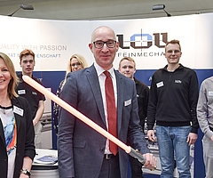 Bürgermeister Dirk Woschei präsentiert ein Lichtschwert, das die Auszubildenden der Firma Loll Feinwerkmechanik gebaut hatten. Die Mitarbeitenden Christina Bichel-Riemer (von links), Matti Fleischer, Wendy Rehder, Philipp Christian Kröning, Andreas Schinkel und Moritz Luck begrüßten ihn am Stand des Tornescher Unternehmens. (Foto: Frank)